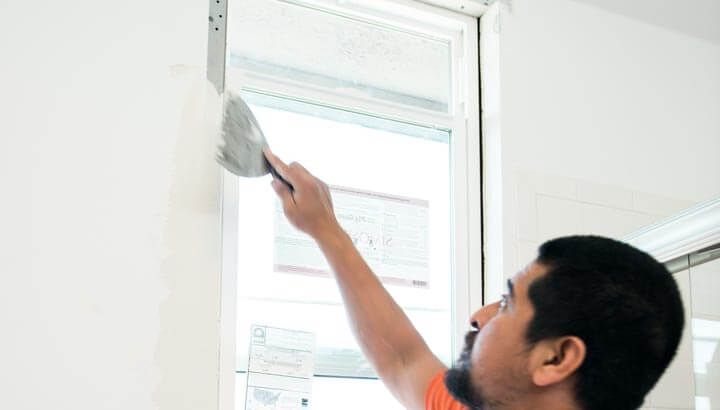 Man layering drywall mud on drywall to complete repair